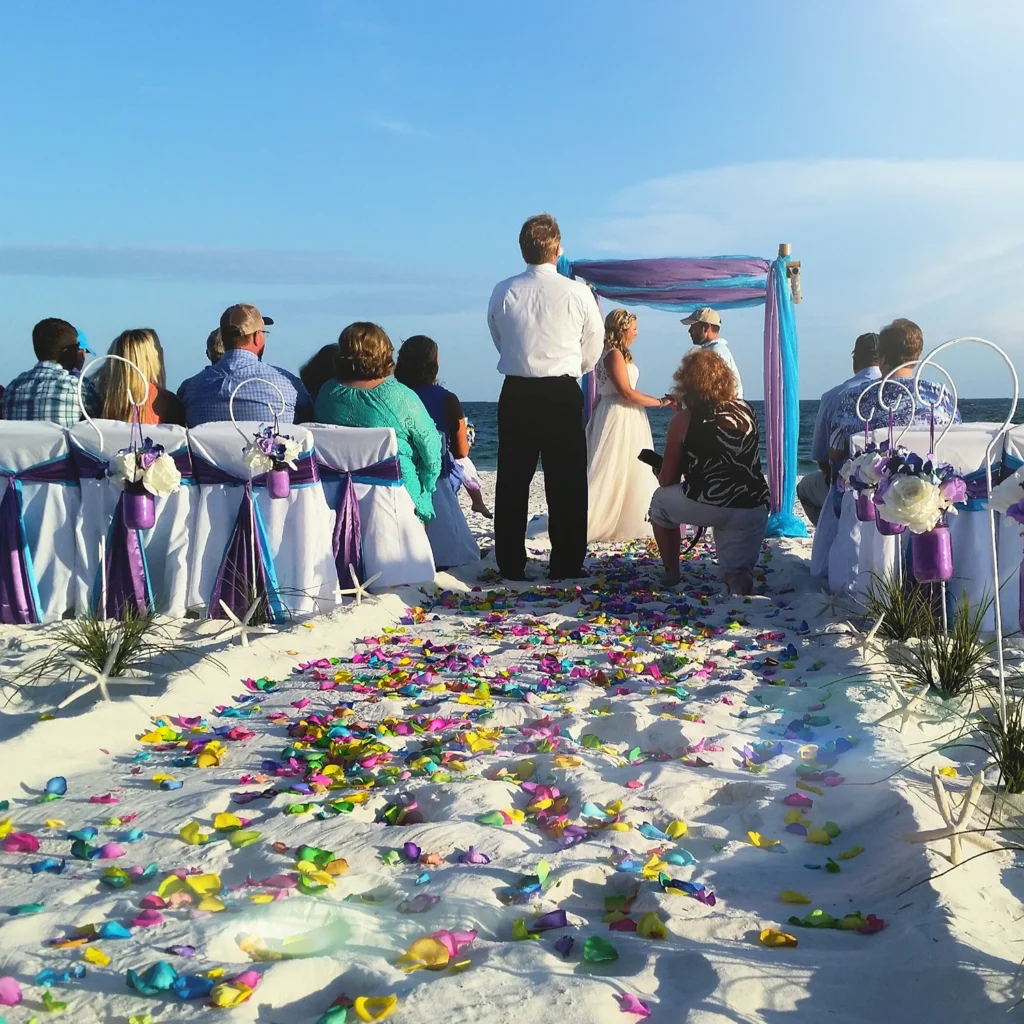 Beach wedding ceremony on Siesta Key with guests seated beside a flower petal aisle leading to a waterfront wedding arch.