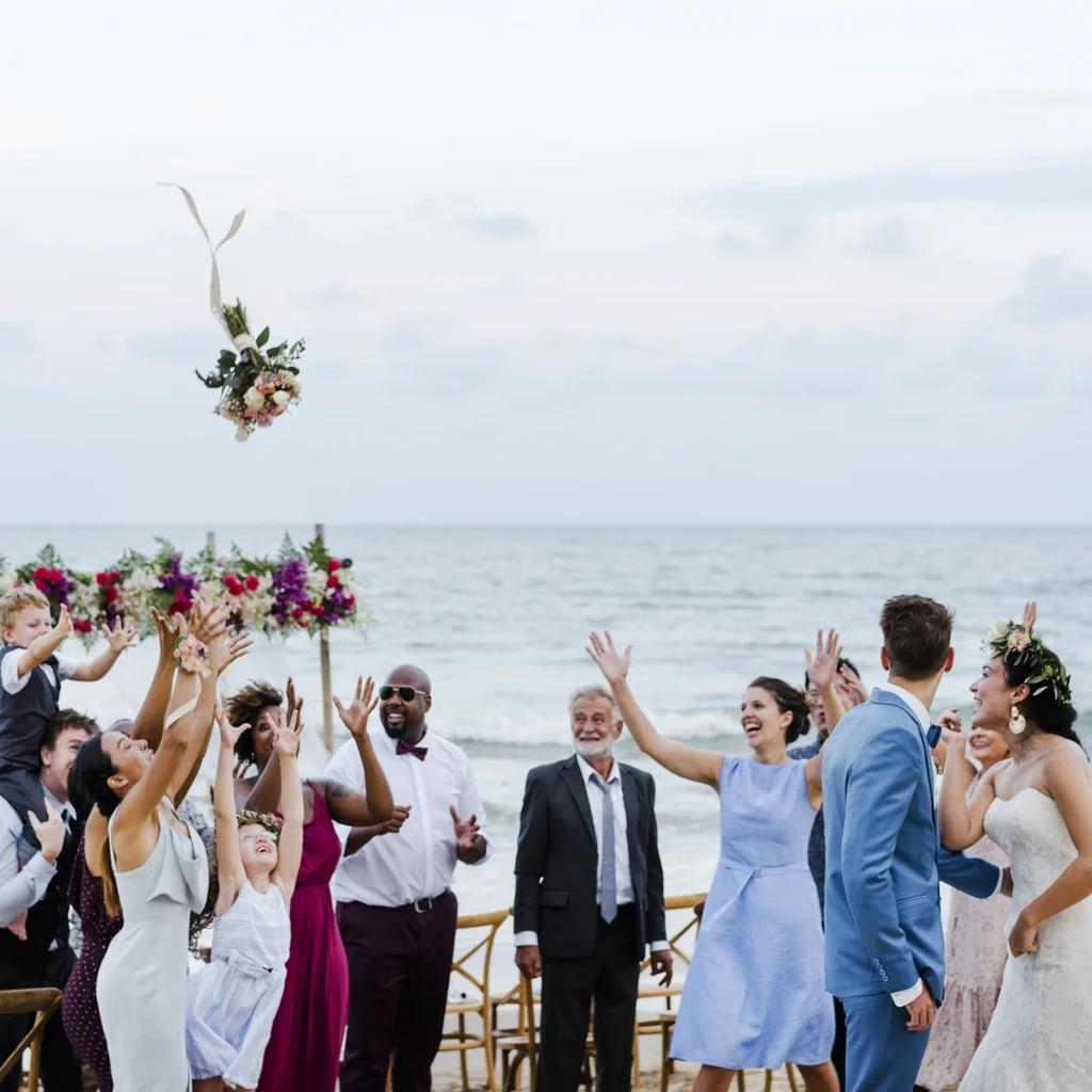 Wedding guests reaching for the bride's bouquet during a joyful beach wedding celebration on the Sarasota waterfront.