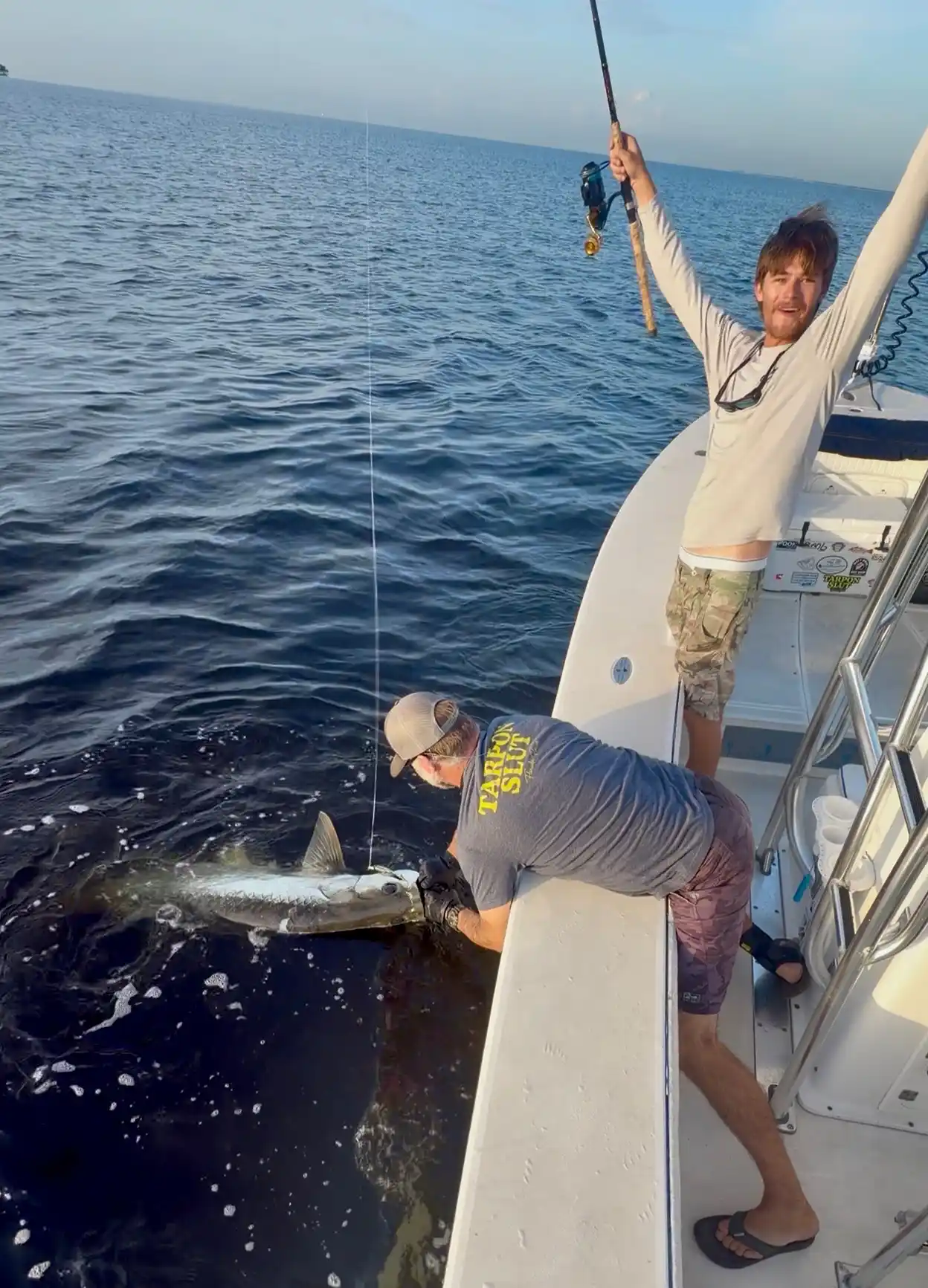 Angler celebrating with his fishing rod raised while another angler holds a tarpon beside the boat near Sarasota, Florida.